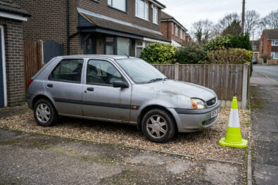 Empty driveway, small hatchback ready for a collection truck, lime cone beside the front wheel.